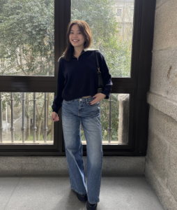 A woman smiling in front of a large window. 
